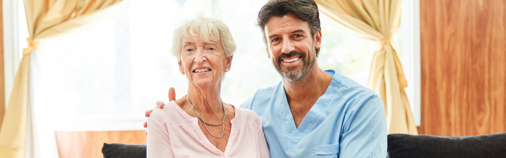 Smiling male nurse and elder woman on a couch